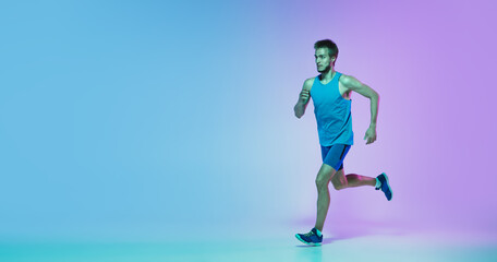 Portrait of young caucasian man running, jogging on gradient studio background in neon light. Professional sportsman training in action, motion. Sport, wellness, activity, concept. Flyer with