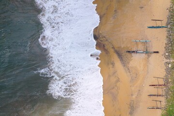 aerial drone bird view shot of the sea shore with turquoise water, an empty yellow sand beach with fishing long boats, white waves and foam forming beautiful textures, patterns, shapes. Sri Lanka