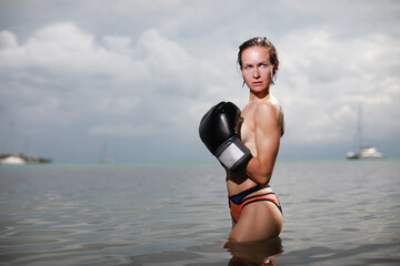 Beautiful woman in black boxing glows and topples naked posing at the Caribbean sea on the beach