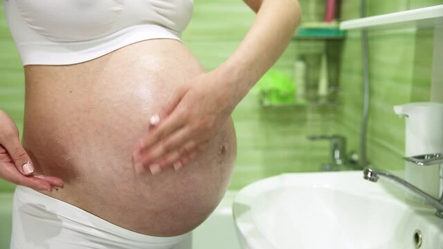 pregnant girl lubricates stomach with cream against stretch marks in the bathroom