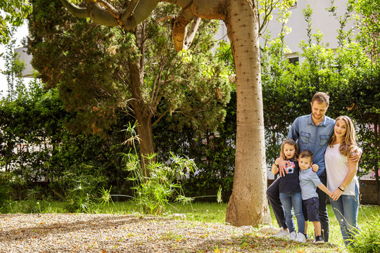 Bellissima famiglia composta da 2 genitori e figli si raduna felice in gruppo nel giardino di casa vicino ad un albero