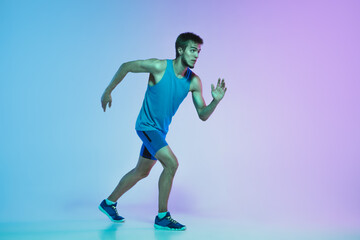 Fototapeta na wymiar Portrait of active young caucasian man running, jogging on gradient studio background in neon light. Professional sportsman training in action and motion. Sport, wellness, activity, vitality concept.