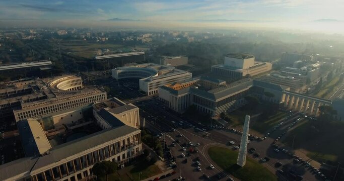 Aerial, drone shot overlooking traffic at the Imperial square and the Obelisk of Marconi, in the EUR district, hazy sunrise, in Rome, Italy