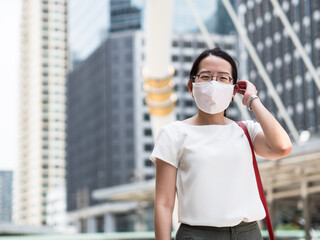 Beautiful Asian women wearing disposable medical face mask, while in a public area, roadside, or city center, as new normal trend and self-protection against Covid19 infection.