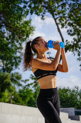 Sporty woman drinks water in park