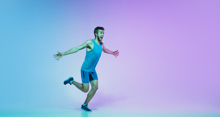 Fototapeta na wymiar The first, winner. Portrait of young caucasian man running, jogging on gradient studio background in neon light. Professional sportsman training in motion. Sport, wellness, activity, concept. Flyer.