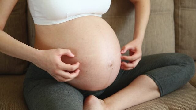 A pregnant woman scratching her belly with her hand. The girl's stomach itches and child pushes in the stomach