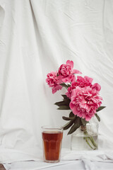 glass with tea and a bouquet of flowers on a white vintage background. flowers red peonies