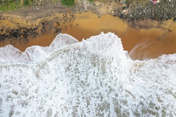 aerial drone bird view shot of the sea shore with yellow sand, black rocks, large white waves and foam crashing on the beach forming beautiful textures, patterns, shapes. Sri Lanka