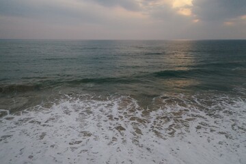 Obraz premium aerial sunset drone bird view shot of the sea surface with turquoise blue water, large white waves and foam forming beautiful textures, patterns, shapes and a cloudy sky on the horizon. Sri Lanka