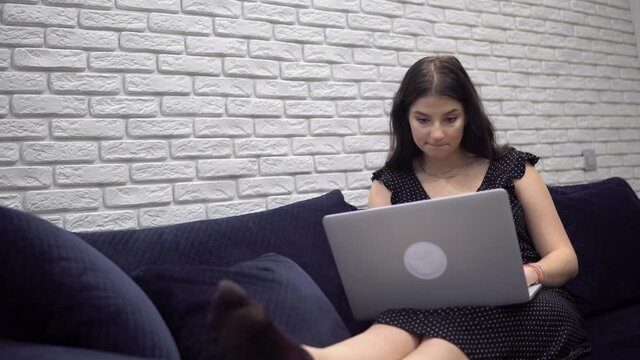 Attractive woman using laptop on sofa couch, relaxing at home, chatiing