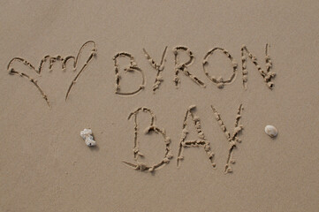 Shaka hand gesture and Byron Bay inscription in the sand