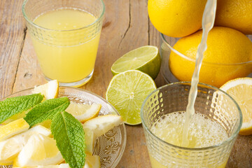 Aerial view of lemon juice falling into a glass, plate with slices, mint, full glass and whole...