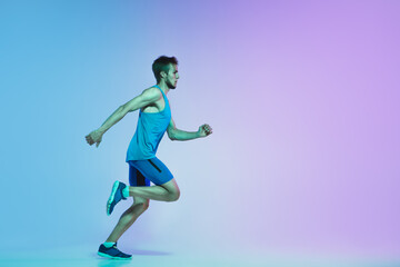 Fototapeta na wymiar In jump. Portrait of young caucasian man running, jogging on gradient studio background in neon light. Professional sportsman training in action and motion. Sport, wellness, activity, vitality concept