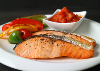 Homemade pan seared salmon steaks with grilled colorful vegetables and salsa on white plate