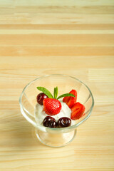 Ice cream dessert with strawberries and cherries in a bowl on a wooden table. Copy space.