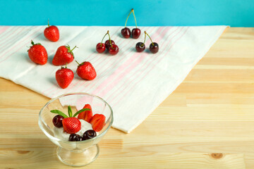 Ice cream dessert with strawberries and cherries in a gourd on a wooden table next to scattered berries.