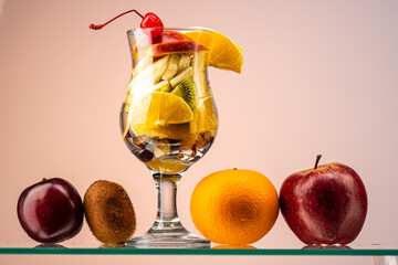 fruit salad of fresh fruits and berries in a transparent glass on a gradient background