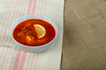Traditional Tom Yum soup with chicken in a plate on a tablecloth on a linen napkin.