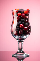 mix of cherries, strawberries and mulberries in a transparent glass on a gradient background