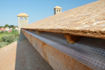 Fototapeta na wymiar A close-up on plywood board, OSB used for roof sheathing installed on roof beams with blurred roofing construction in the background.