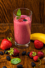 smoothie of berries, banana, milk in a transparent glass on a background of components
