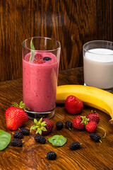 smoothie of berries, banana, milk in a transparent glass on a background of components