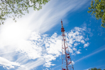 Obraz premium red tall television tower on a background of blue sky and clouds and green trees