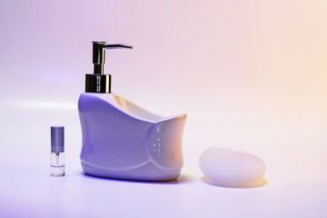 Liquid soap dispenser in a ceramic bath with a sponge and a spray jar, in purple night light