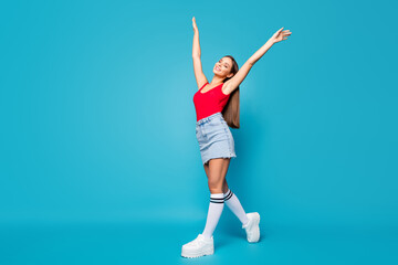 Full body profile side photo of calm cheerful satisfied youth lady go walk enjoy spring wind air raise hands arms wear tank-top gumshoes isolated over blue color background