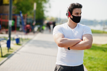 Portrait sports arabian man in black medical face mask posed outdoor with earphones during coronavirus quarantine.