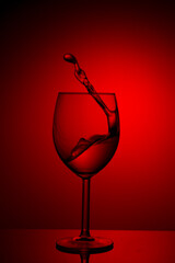 A splash of red wine in a glass on a red background