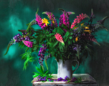 Classic still life with beautiful bouquet of purple and pink lupin flowers in old vintage white jug on old wooden white table in ray of light on green background. Art photography.