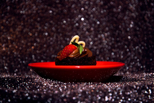 Chocolate cupcake with strawberry on a red plate, silver glitter backgroud