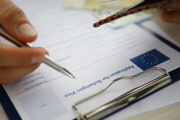 Close-up of male person filling application form for schengen visa holding silver pen. Writing personal information on paper. Travelling abroad or immigration concept