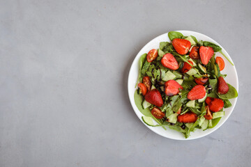Fototapeta na wymiar Plate of fresh vegetarian salad with strawberry, spinach, cucumber on the gray background. Copy space.
