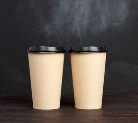 two brown paper disposable cups with a plastic lid stand on a wooden table