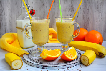 Delicious banana-citrus milkshake with bright straws and slices of orange and banana on a light background. Healthy lifestyle.