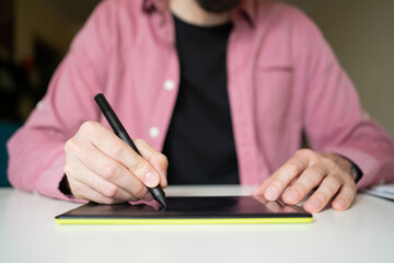 Unrecognizable focused guy drawing on graphic tablet. Male hands holding stylus and electronic...