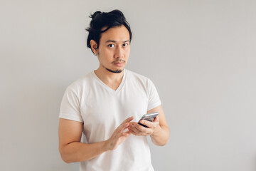 Long hair Asian man in white casual t-shirt is using smartphone.