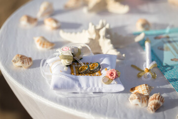 Decorated small white pillow (with roses and shells around) with wedding gold rings