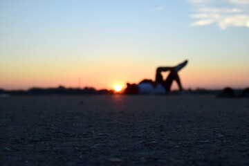 Blurred image of people lying on the concrete floor for recreation near to natural water pond at sunset time isolated with orange color of sky light.