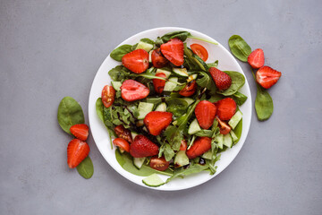 Fototapeta na wymiar Tasty summer salad made of strawberries, arugula, spinach, little tomatoes, cucumbers and balsamic sauce. Top view, flat lay.