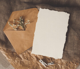 Cerastium dry flower, white empty paper sheet, envelope on natural brown craft sackcloth fabric and crumpled paper flat layout flat-lay top view. Design template for card, invitation, wedding decor