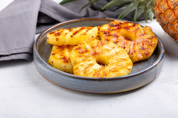 Heap of grilled pineapple slices on gray plate on concrete background.