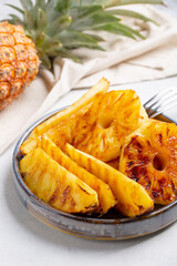 Heap of grilled pineapple slices on gray plate on concrete background.