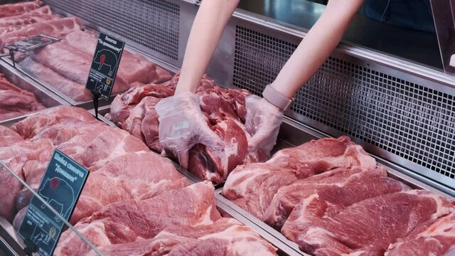 KYIV, UKRAINE – JUNE/03/2020: The seller takes the pork shoulder from the counter.