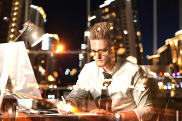 Double exposure of young man working in office and night cityscape. Financial analytics