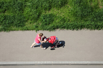 Woman with a baby walking on a sidewalk at summer, top view. Concept of motherhood, single mom with child