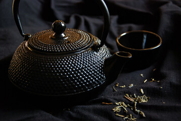 Obraz na płótnie Canvas Chinese tea pot and cup on black background with loose green tea leaves